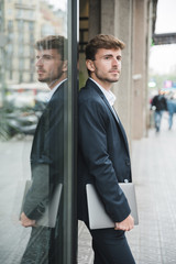 Businessman leaning confidently on a dark glass wall holding digital tablet in hand