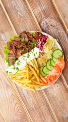 Shawarma plate with beef, french fries, vegetables and sauce close-up on a wooden table. vertical top view from above. Flat lay