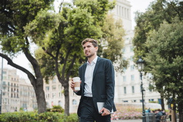 Portrait of a young businessman standing in front of building holding takeaway coffee cup and digital tablet