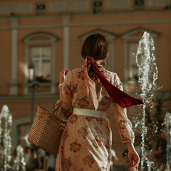 Rear, back view of fashionable woman wearing pink dress, trendy hair scarf, holding straw wicker bag. Elegant summer, spring outfit, street fashion concept