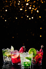 Four colorful tasty alcoholic cocktails in a row at the bar stand. Luxury vacation concept. Place for text. Vertical. Festive holiday bokeh