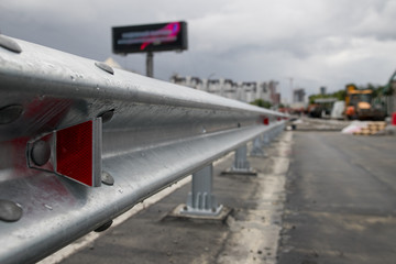 Fototapeta premium Red road reflectors along the road. Zinked or galvanized metal road fencing of barrier type, close-up. Road and traffic safety. Selective focus with shallow depth of field.
