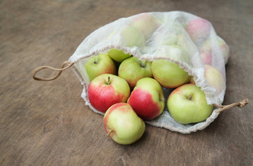 Zero waste shopping concept. Fresh organic apples in reusable mesh produce bag on wooden table