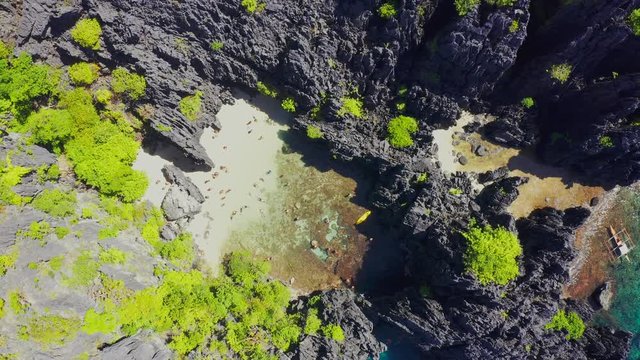 Aerial drone view of swimmers inside a tiny hidden tropical lagoon surrounded by cliffs - Secret Lagoon, Miniloc island in El Nido, Palawan, Philippines