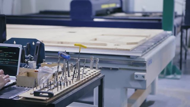 Tracking shot of laser engraving machines in cnc laboratory and unrecognizable female technician in white coat working on laptop computer surrounded by work tools