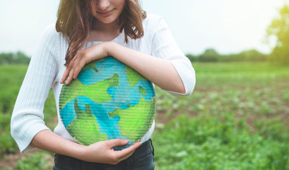 Teen girl holding planet in hands against green spring background. Earth day holiday concept....