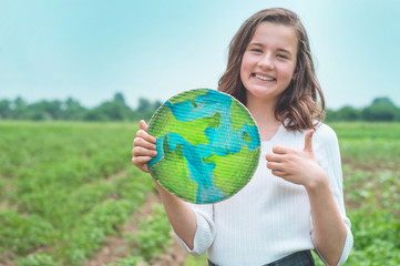 Teen girl holding planet in hands against green spring background. Earth day holiday concept. Protection and love of earth