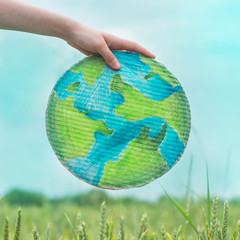 Teen girl holding planet in hands against green spring background. Earth day holiday concept. Protection and love of earth