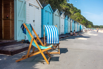 Folding deck chairs sat outside a line of beach huts on Avon Beach at Mudeford in Dorset, UK