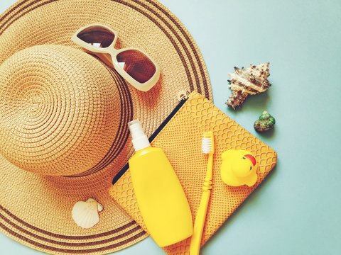 Flat lay summer travel photo, beach essentials. Sun hat, sunglasses, cosmetic bag, sunscreen bottle, toothbrush, seashells and rubber duck