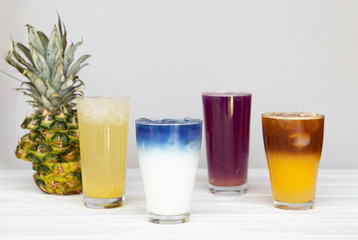 assortment of fresh iced fruit drinks on a white background with chopped slices of pineapple and orange, closeup