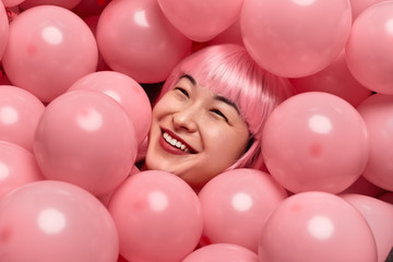 Fototapeta na wymiar Cheerful Asian lady lying under pink balloons