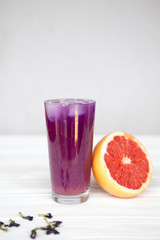 a high glass filled with a cold summer drink of purple in the background of a threaded grapefruit