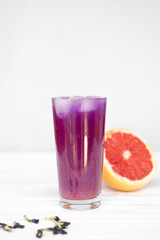 a high glass filled with a cold summer drink of purple in the background of a threaded grapefruit