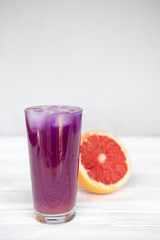 a high glass filled with a cold summer drink of purple in the background of a threaded grapefruit