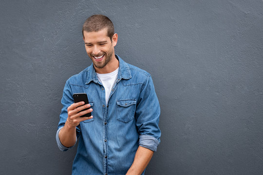 Cool smiling man using smartphone on grey wall - Powered by Adobe