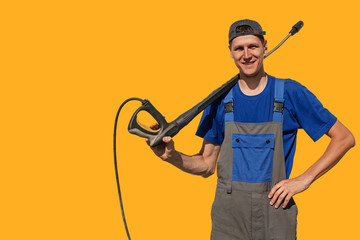 Tall slim guy with a gun for a car wash isolated on yellow background. A worker in coveralls looks...