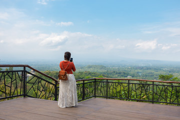 Woman taking photo with her phone of scenic countryside from a lookout.