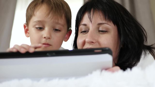 Portrait of a woman and a child. A mother and a little boy use a tablet computer to call, watch a movie, and access the Internet.