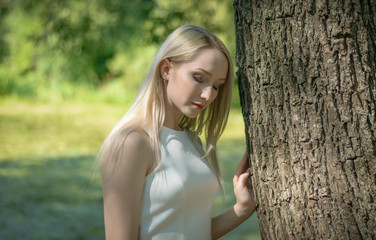 Young woman in the forest is sitting on a fallen tree with dandelion on her hand. Unity with nature.