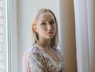 Pensive woman in bathrobe sitting on the windowsill. Natural light.