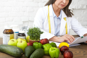 Obraz premium Food, nutrition, health, wellbeing and dietology concept. Elderly female nutritional expert with measuring tape around her neck developing dietary plan to improve eating habits of her client