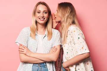 Pleased smiling beautiful blondes women friends posing isolated over pink wall background talking with each other gossiping.