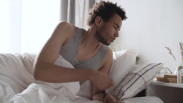 Young black man getting up early in the morning, lying on bed and using mouth spray