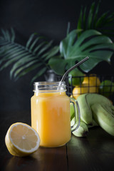 Fresh summer fruits juice with banana, lemon on dark tropical background. Close up.