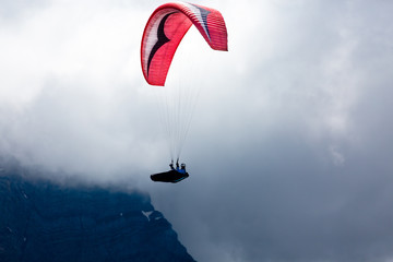 Red paraglider with dark clouds, fog and mointains in background