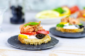 small canape with pink salmon fish, cucumber, tomato, olive and lemon on a light wooden background
