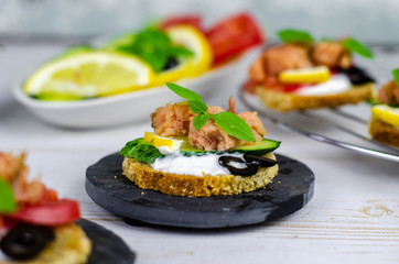 small canape with pink salmon fish, cucumber, tomato, olive and lemon on a light wooden background