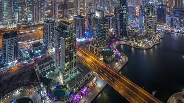 Aerial top view of Dubai Marina night timelapse. Promenade and canal with floating yachts and boats in Dubai, UAE. Illuminated modern towers and traffic on the road