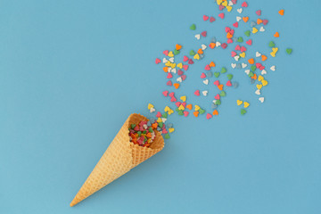 Ice cream cone with colorful sprinkles on blue background. Multiple colored sprinkle dots hearts....