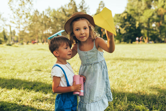 Image of two kids playing with a binoculars and paper plane in summer day in park. Happy sister and brother playing pretend safari game outdoors in the forest. Childhood concept