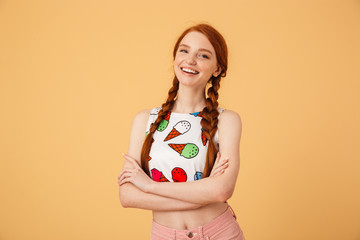 Excited beautiful redhead woman dressed in ice cream printed t-shirt posing isolated over yellow background.