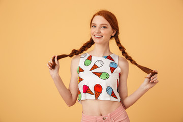 Cheerful beautiful redhead woman dressed in ice cream printed t-shirt posing isolated over yellow...