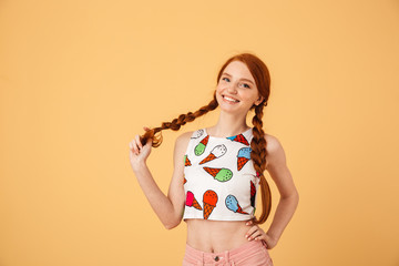 Pleased beautiful redhead woman dressed in ice cream printed t-shirt posing isolated over yellow...