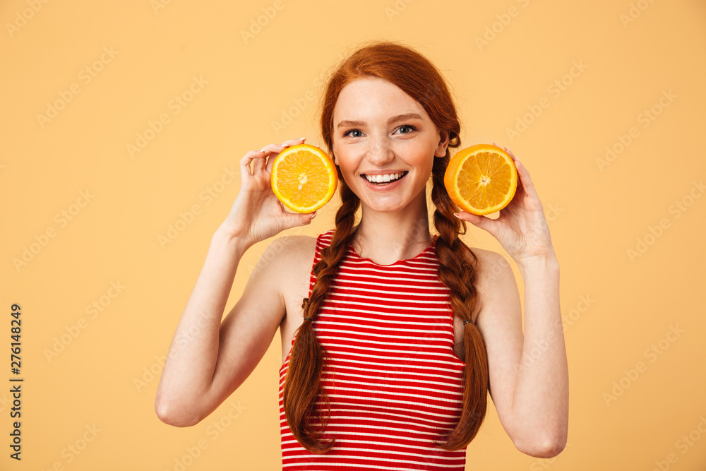 Poster Cheerful  young beautiful redhead woman posing isolated over yellow background holding orange.