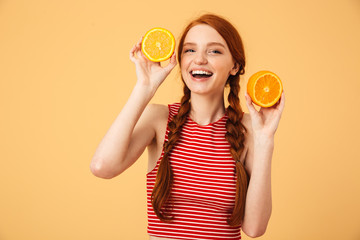 Cheerful  young beautiful redhead woman posing isolated over yellow background holding orange.