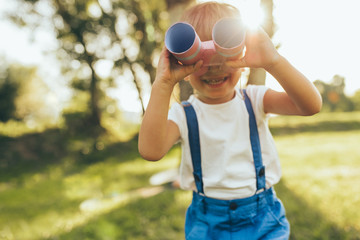 Outdoors closeup portrait of little boy playing with a binoculars searching for an imagination or...