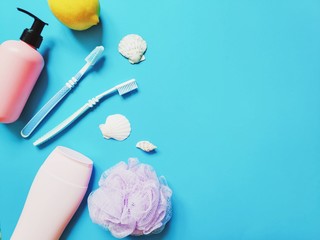 Liquid soap in pink package, two toothbrushes, shampoo bottle, sponge and seashells on a blue background. Flat lay family bathroom stuff