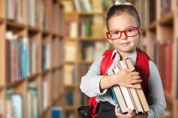 Cute little schoolgirl in glasses on library background