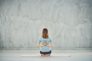 Rear view of Caucasian brunette kneeling on exercise mat and meditating.