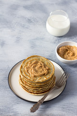 Vegan pancakes with flax seeds, peanut butter and vegan milk on a white plate on a gray background. delicious homemade healthy food	