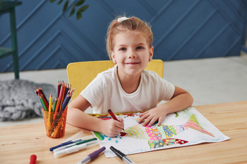 Cute little girl in art school draws her first paintings by pencils and markers