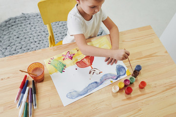 Picking brown color. Little girl is drawing by using gouache and brush. Learning in the art class