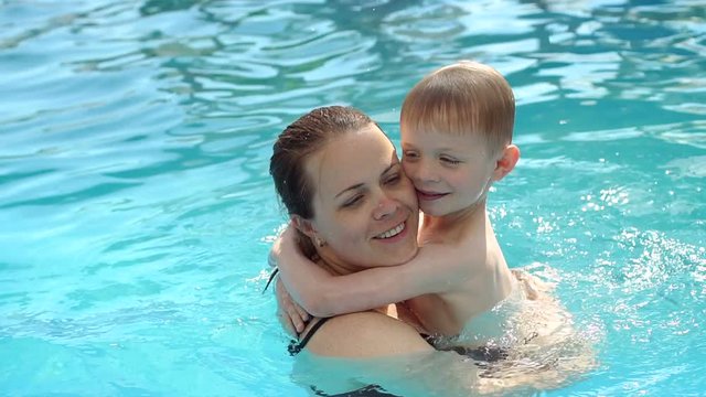 Portrait of a happy mother hugging her son while swimming in the pool on vacation at the hotel. Mom and baby swim in the pool and enjoy the vacation. Slow motion.