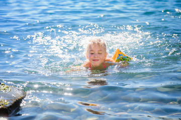 Fototapeta na wymiar Child with inflatable ring on beautiful beach. Little girl swimming in exotic sea. Ocean vacation with kid. Children play on summer beach. Water fun. Kids swim. Family holiday on tropical island.