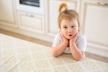 Fototapeta premium Beautiful blonde baby girl having breakfast in kitchen. Funny faces